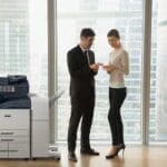 Dos personas en una oficina vestidas de negocios discutiendo documentos junto a una impresora multifunción Xerox® AltaLink® serie B8200 Dos personas en una oficina vestidas de negocios discutiendo documentos junto a una impresora multifunción Xerox® AltaLink® serie B8200
