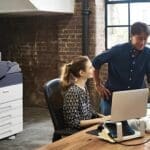 Un hombre y una mujer están uno al lado del otro frente a una computadora, concentrados en la pantalla. La impresora a color Xerox® VersaLink® C7000 está en el fondo. Un hombre y una mujer están uno al lado del otro frente a una computadora, concentrados en la pantalla. La impresora a color Xerox® VersaLink® C7000 está en el fondo.