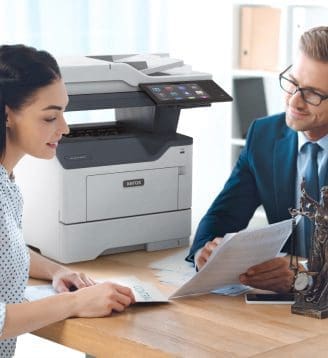 Un hombre y una mujer sentados a una mesa conversan mientras hay una impresora Xerox® cerca.
