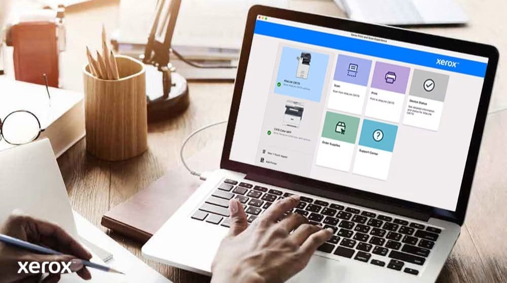 Las manos de una persona están sobre el teclado de una computadora portátil y la pantalla muestra la interfaz de Xerox Print and Scan Experience con opciones como Escanear, Imprimir, Estado del dispositivo, Solicitar suministros y Centro de soporte, lo que indica un control fácil de usar.
