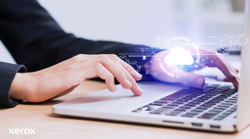 Se muestran las manos de una persona escribiendo en el teclado de una computadora portátil, con un ícono de nube brillante y conexiones de red superpuestas sobre la imagen, simbolizando la conectividad en la nube y los flujos de trabajo digitales.